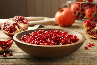 Photo of Ripe juicy pomegranate grains in bowl on wooden table, closeup