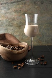 Photo of Coffee cream liqueur in glass and beans on black wooden table