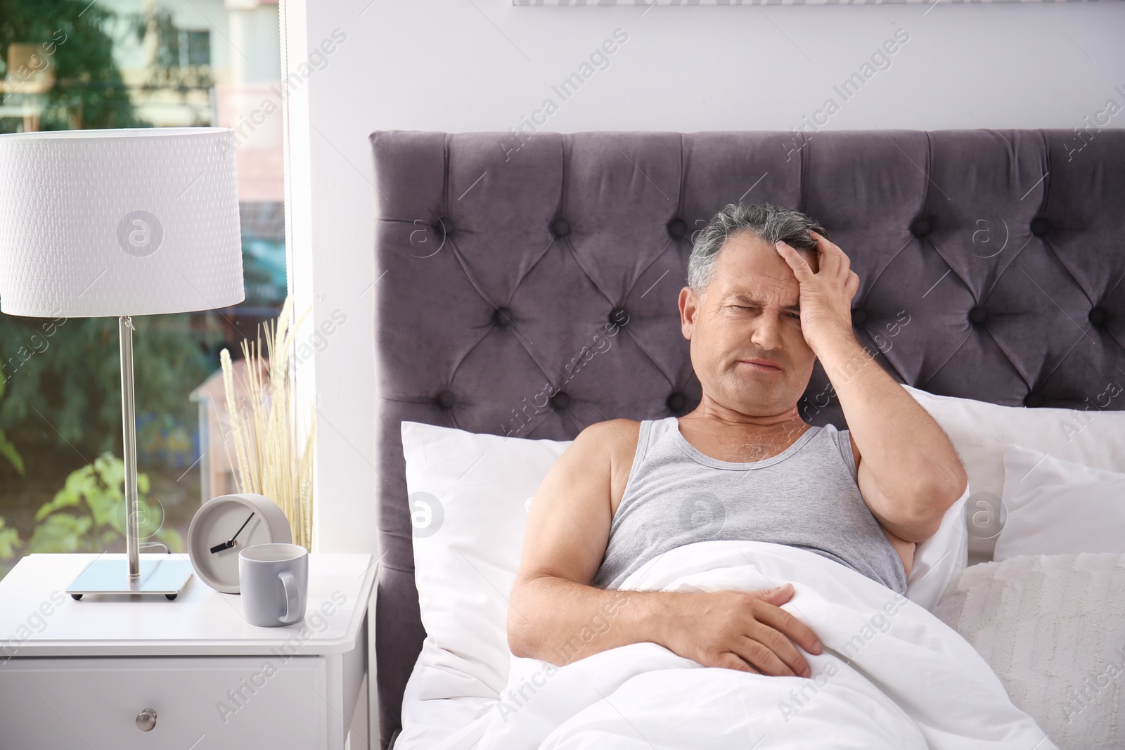 Photo of Man suffering from headache after sleep in bed. Uncomfortable pillow