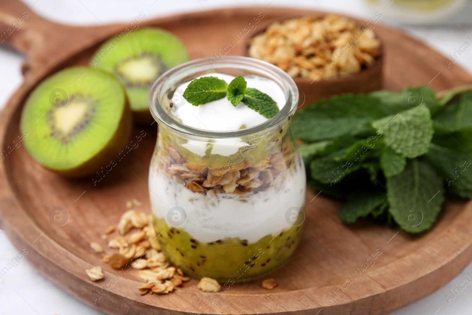 Photo of Delicious dessert with kiwi, yogurt and muesli on wooden board, closeup