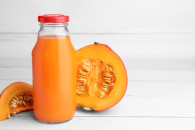 Photo of Tasty pumpkin juice in glass bottle and cut pumpkin on white wooden table. Space for text