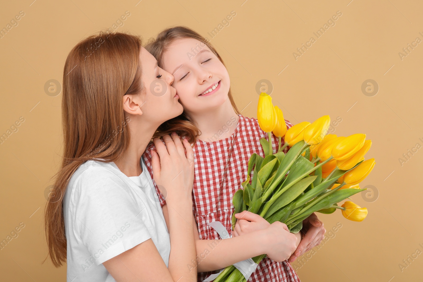 Photo of Mother and her cute daughter with bouquet of yellow tulips on beige background