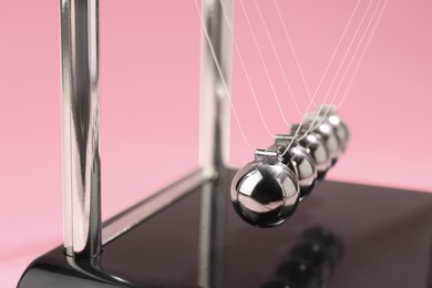 Photo of Newton's cradle on pink background, closeup. Physics law of energy conservation