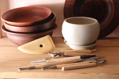 Set of different crafting tools and clay dishes on wooden table in workshop