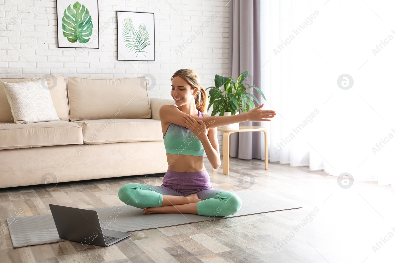 Photo of Woman having online video class via laptop at home. Distance yoga course during coronavirus pandemic