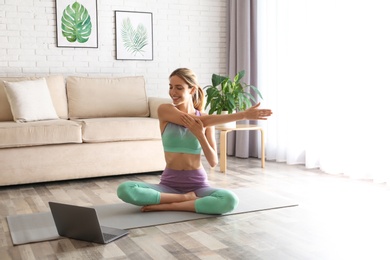 Photo of Woman having online video class via laptop at home. Distance yoga course during coronavirus pandemic