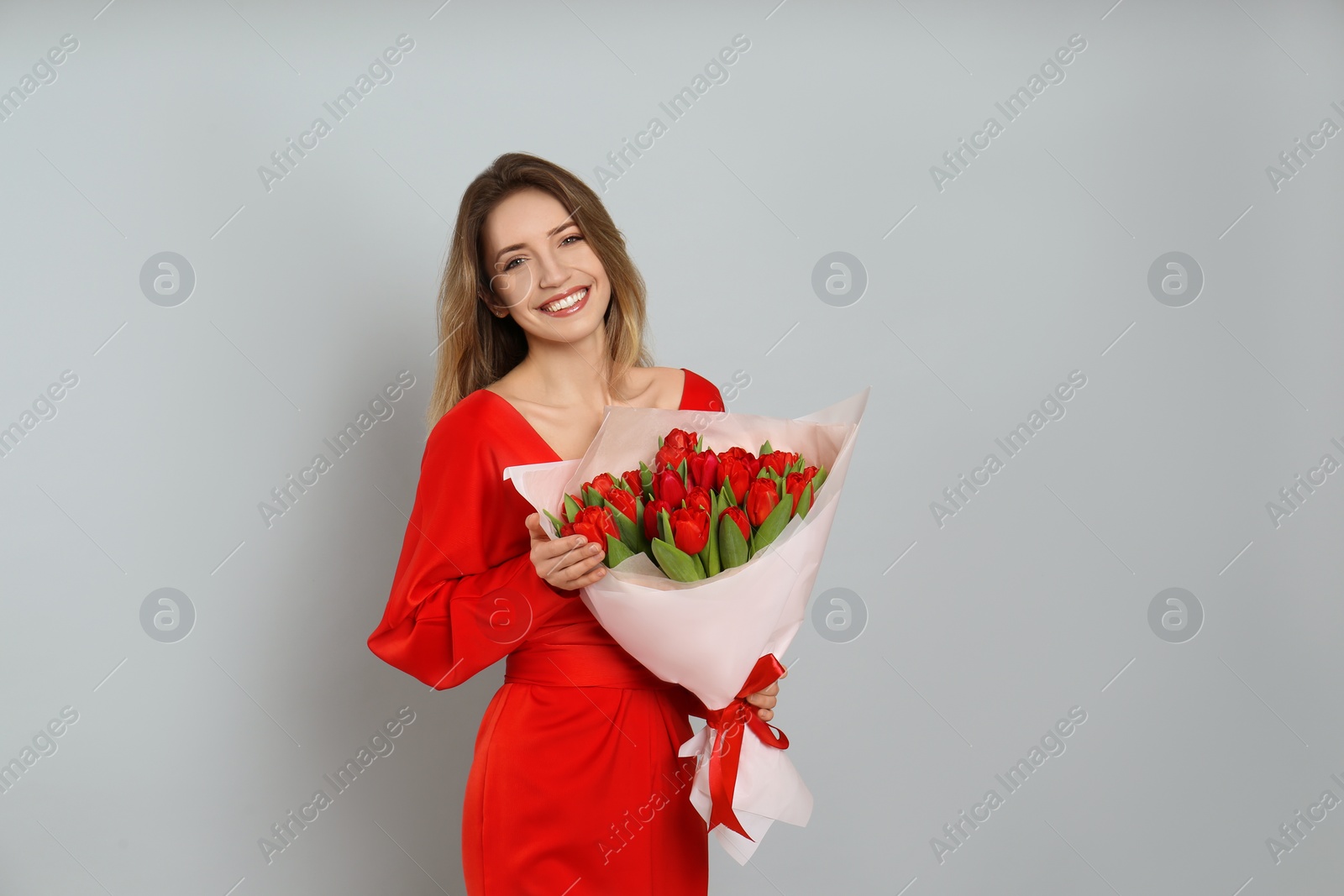 Photo of Happy woman with red tulip bouquet on light grey background, space for text. 8th of March celebration