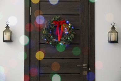 Beautiful Christmas wreath with red bow and festive lights hanging on door