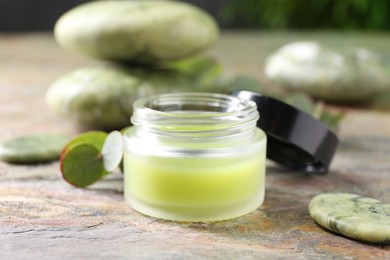 Photo of Jar of cream and spa stone on textured table, closeup. Body care product