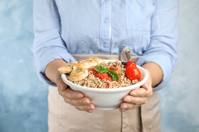 Photo of Woman holding bowl with tasty buckwheat porridge and meat on light blue background, closeup