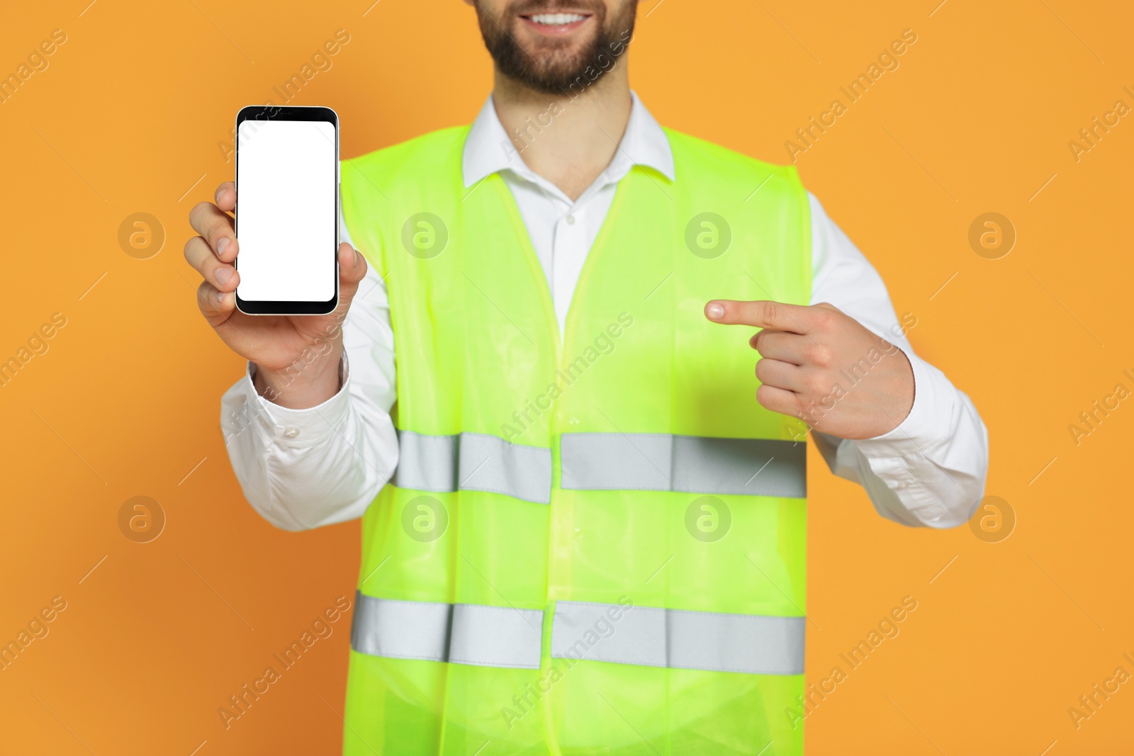 Photo of Man in reflective uniform showing smartphone on orange background, closeup