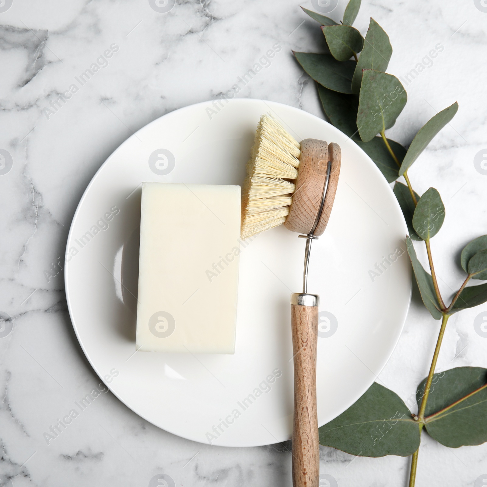 Photo of Cleaning supplies for dish washing, plate and eucalyptus branch on white marble table, flat lay