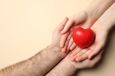 Photo of Couple holding red heart on beige background, top view