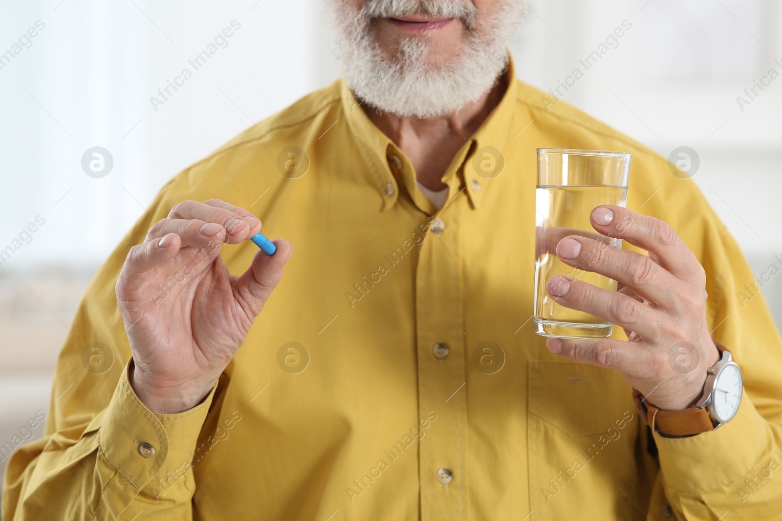 Photo of Senior man with glass of water and pill indoors, closeup