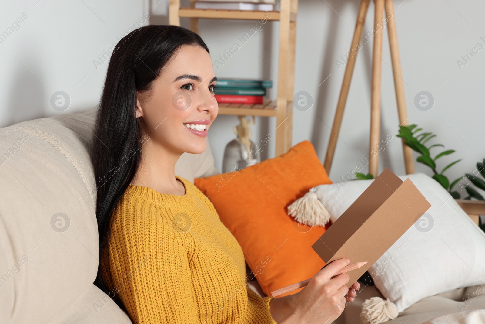 Photo of Happy woman reading greeting card on sofa in living room