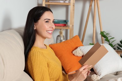 Happy woman reading greeting card on sofa in living room