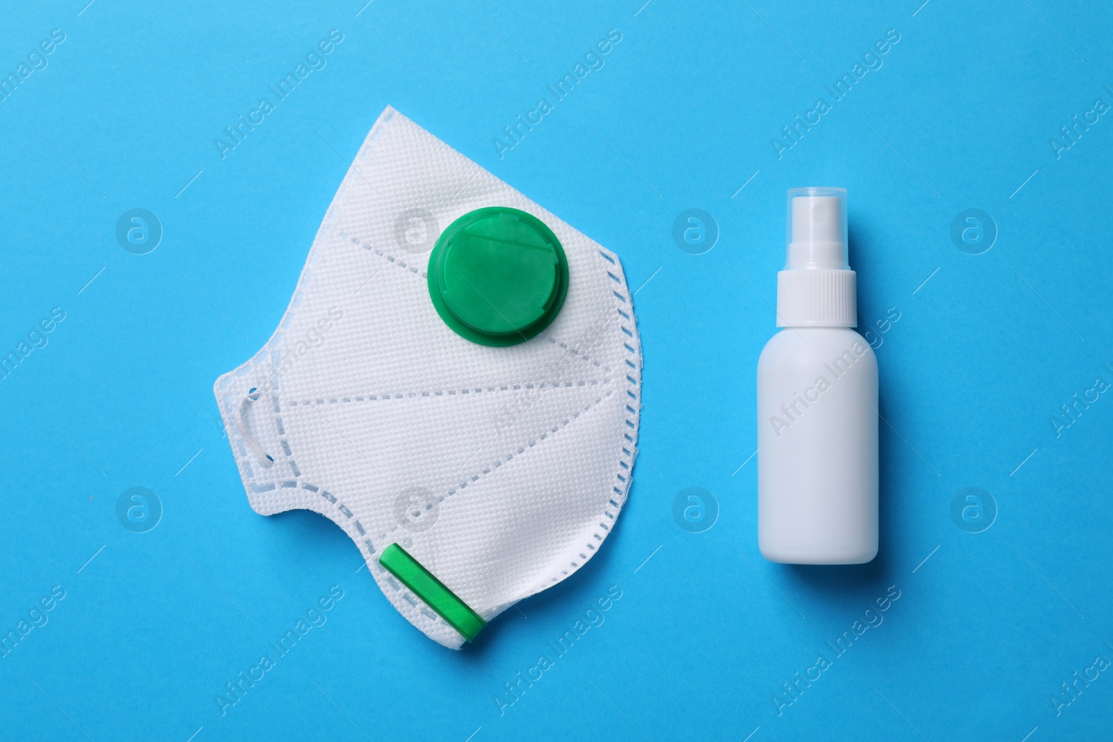 Photo of Hand sanitizer and medical respirator on light blue background, flat lay