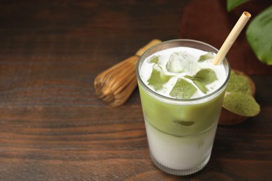 Glass of tasty iced matcha latte, bamboo whisk and powder on wooden table. Space for text