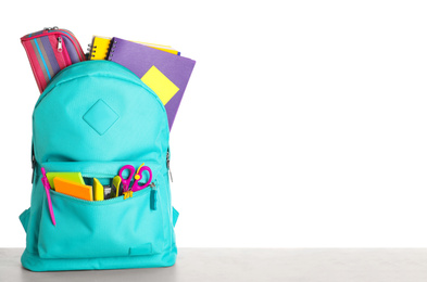 Bright backpack with school stationery on grey stone table against white background