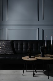 Photo of Elegant leather sofa and candlesticks on coffee table near light grey wall. Interior design