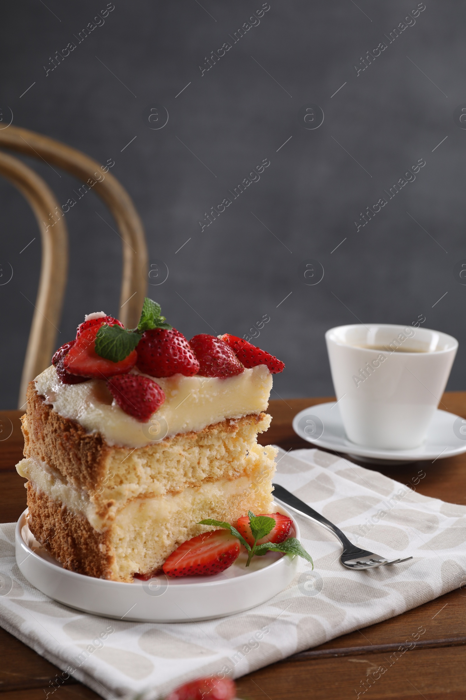 Photo of Piece of tasty cake with fresh strawberries, mint and cup of tea on wooden table