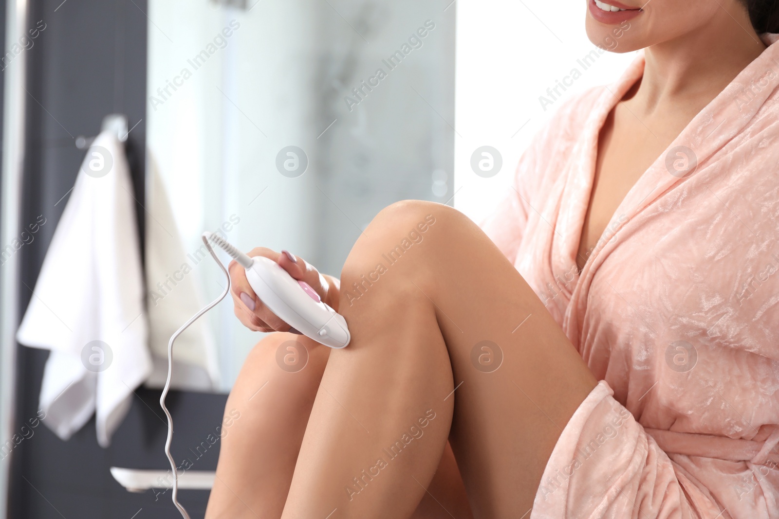 Photo of Young woman epilating her legs in bathroom, closeup