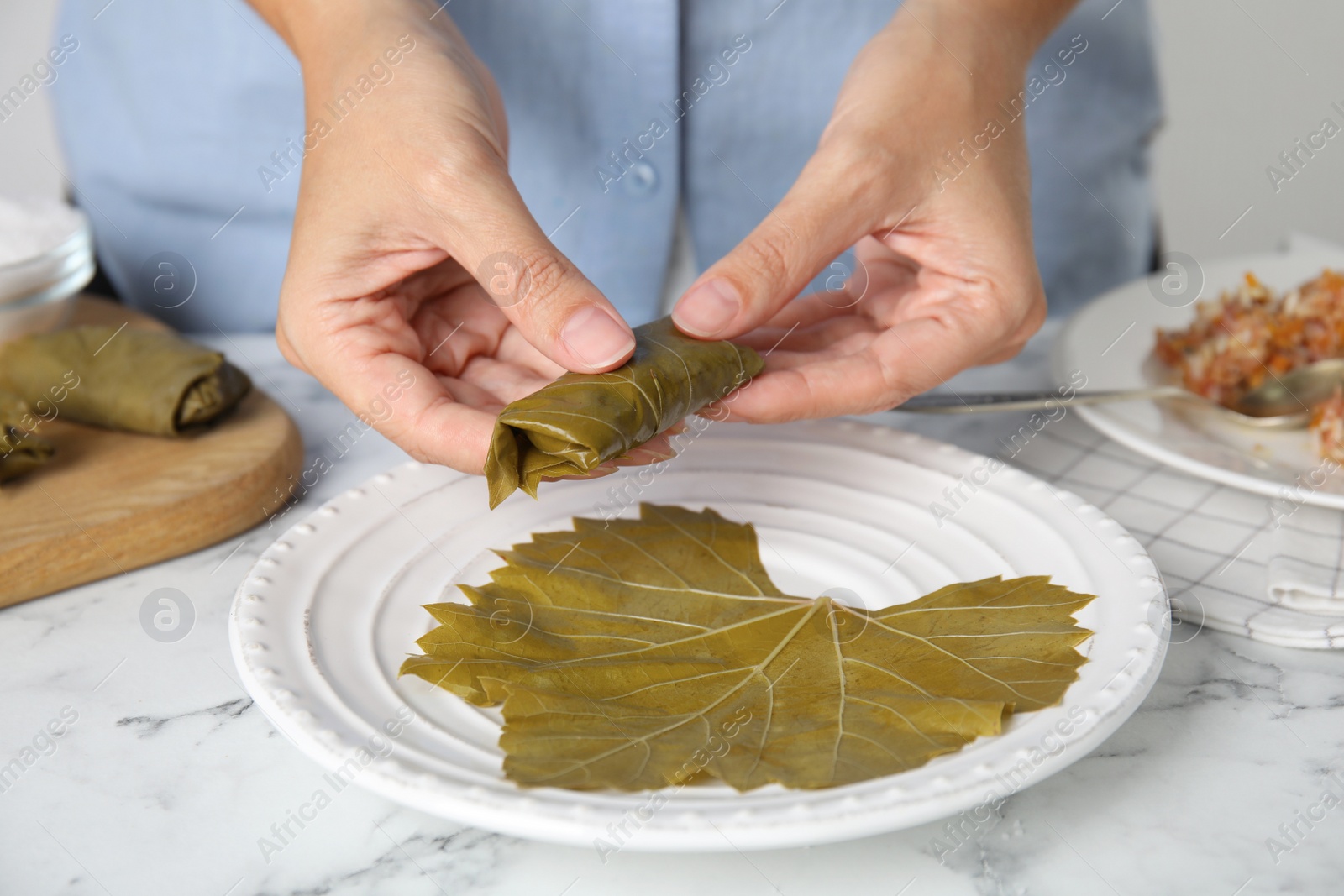 Photo of Woman preparing stuffed grape leaves at white marble table, closeup