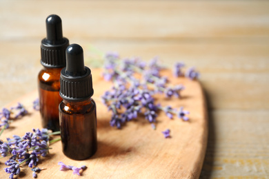 Photo of Bottles of essential oil and lavender flowers on wooden table. Space for text