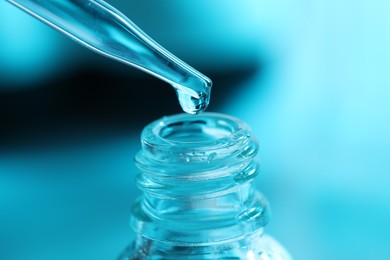 Photo of Dripping liquid from pipette into glass bottle on light blue background, closeup