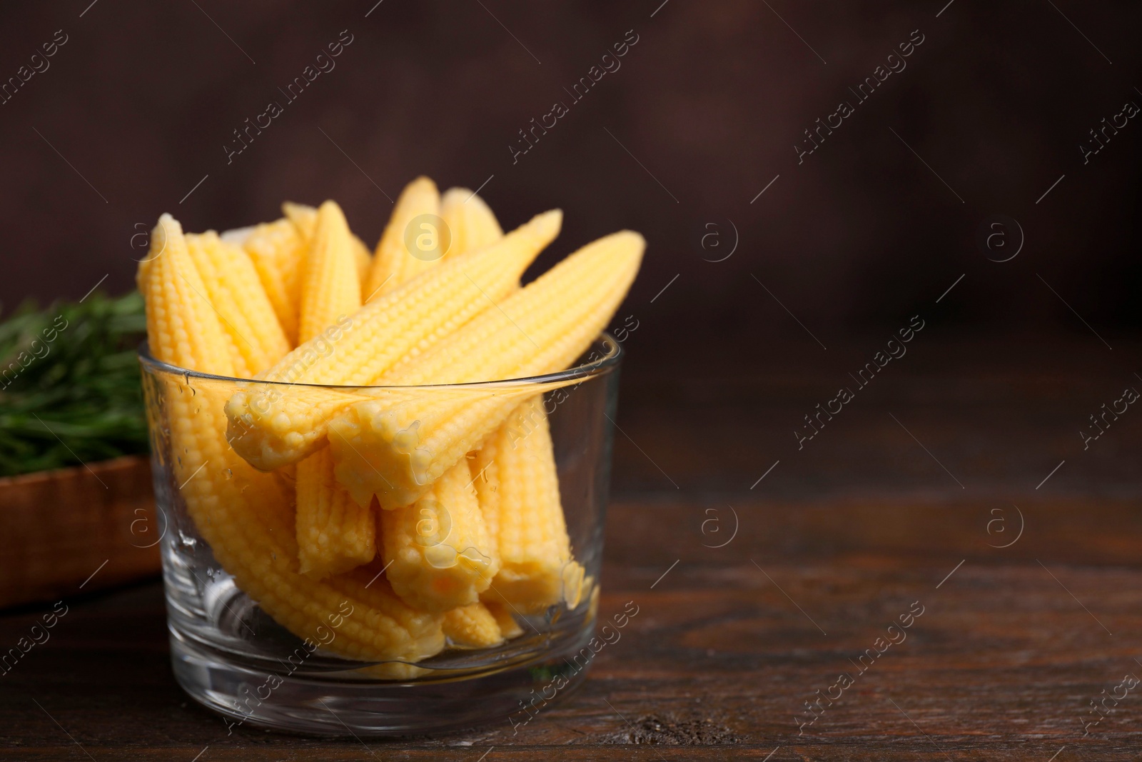 Photo of Tasty fresh yellow baby corns in glass on wooden table, space for text