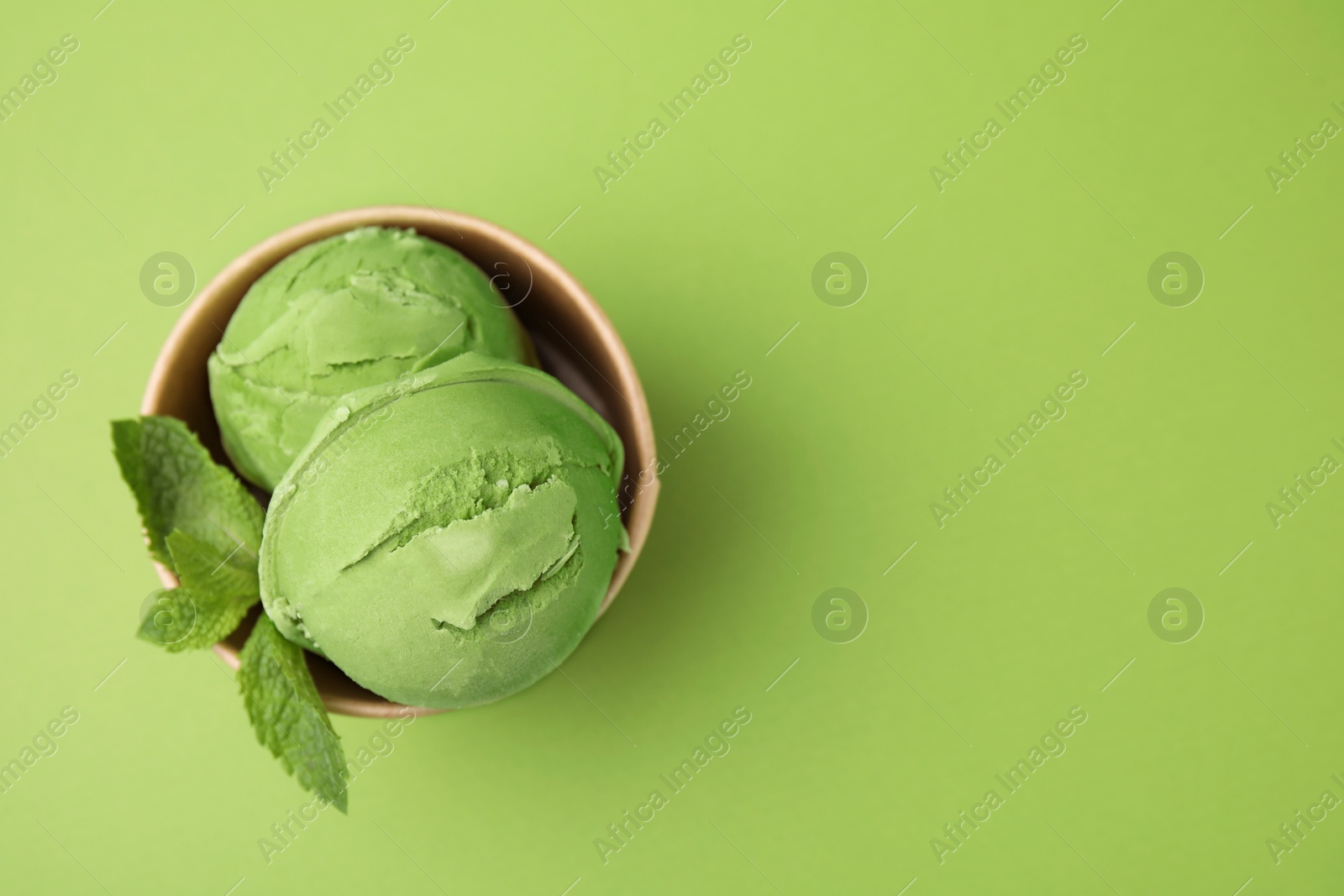 Photo of Paper cup with tasty matcha ice cream on light green background, top view. Space for text