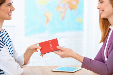 Photo of Female manager giving passport with ticket to client in travel agency