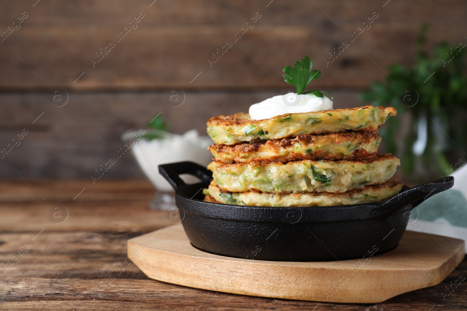Photo of Delicious zucchini fritters with sour cream on wooden table, closeup. Space for text