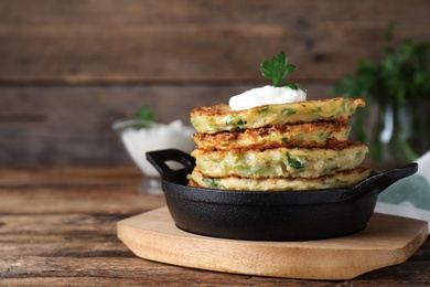 Photo of Delicious zucchini fritters with sour cream on wooden table, closeup. Space for text