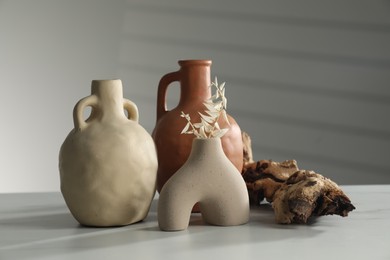 Clay flagons, vase, dried flowers and wooden snag on white marble table