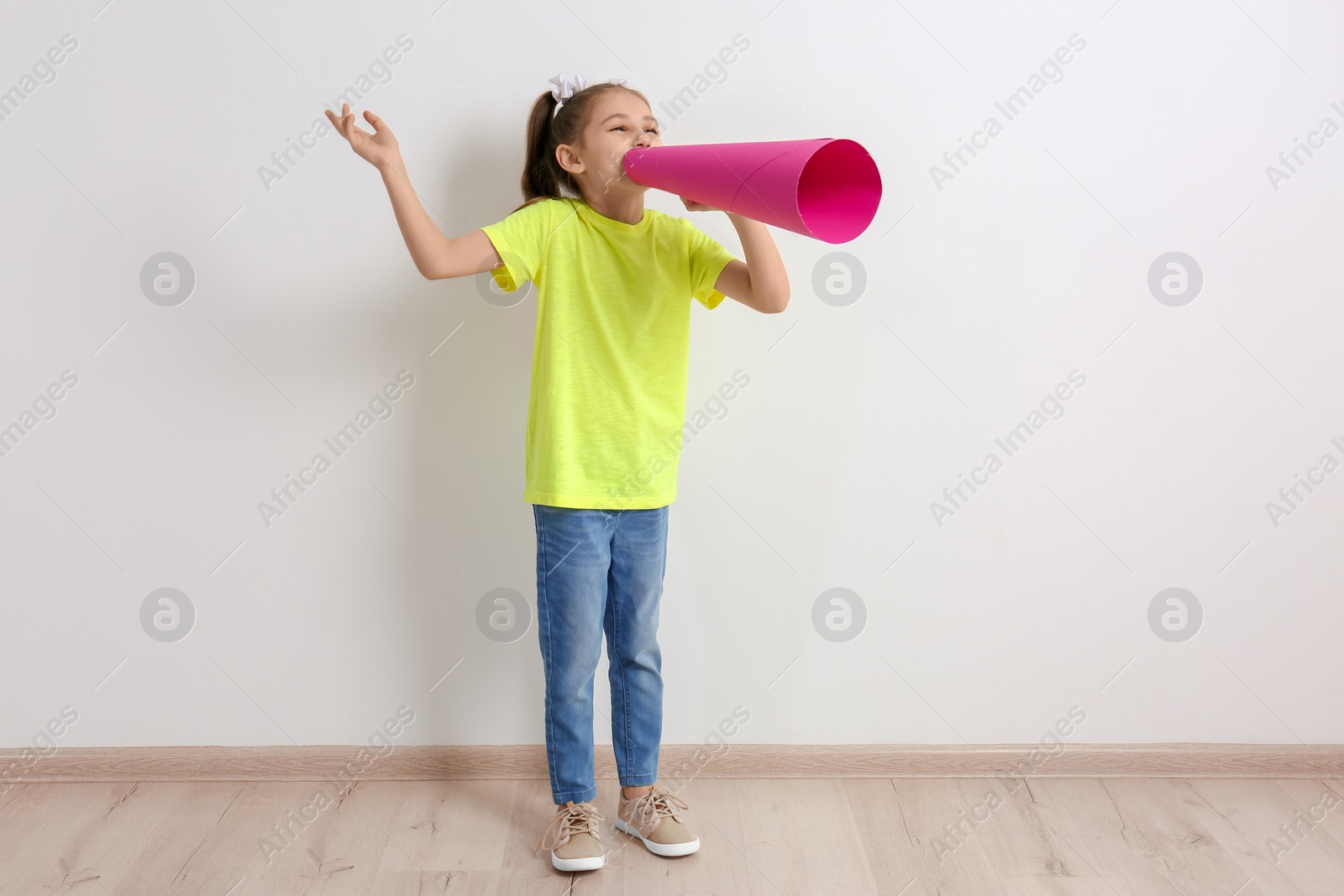 Photo of Cute little girl with paper megaphone near white wall