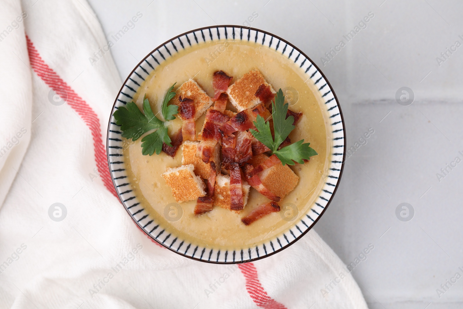 Photo of Delicious lentil soup with bacon and parsley in bowl on white tiled table, top view