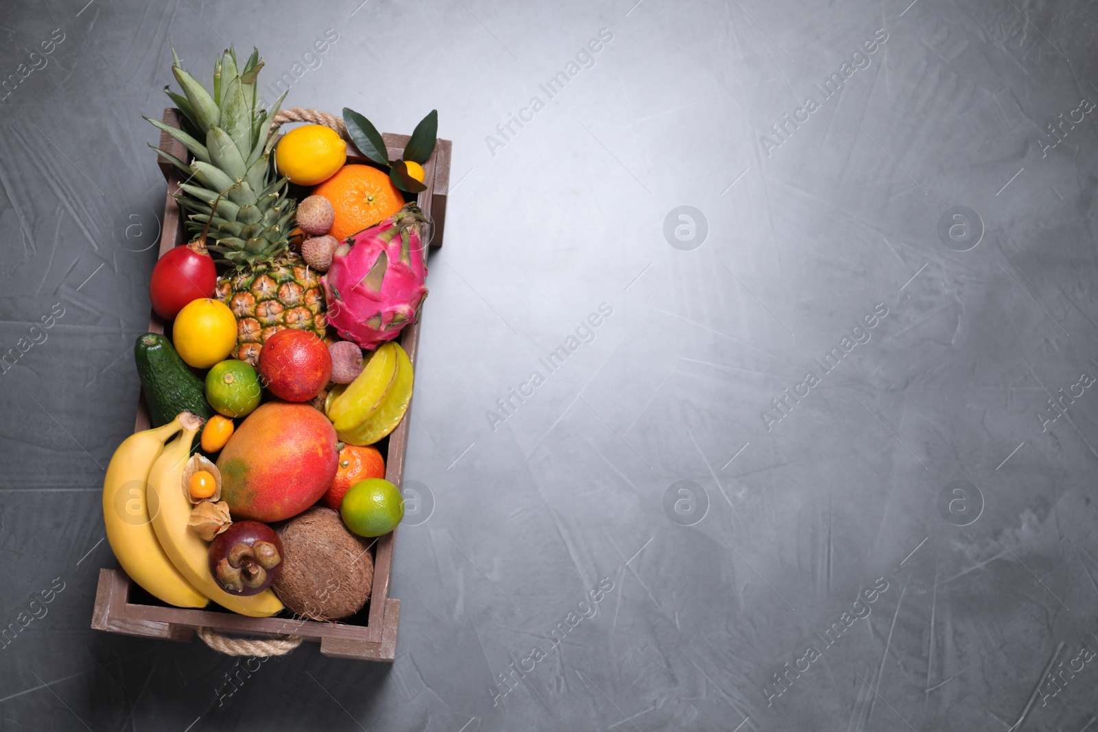 Photo of Different tropical fruits in wooden box on grey background, top view. Space for text