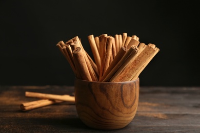 Photo of Aromatic cinnamon sticks on wooden table against black background