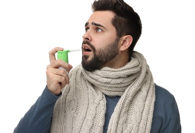 Young man with scarf using throat spray on white background