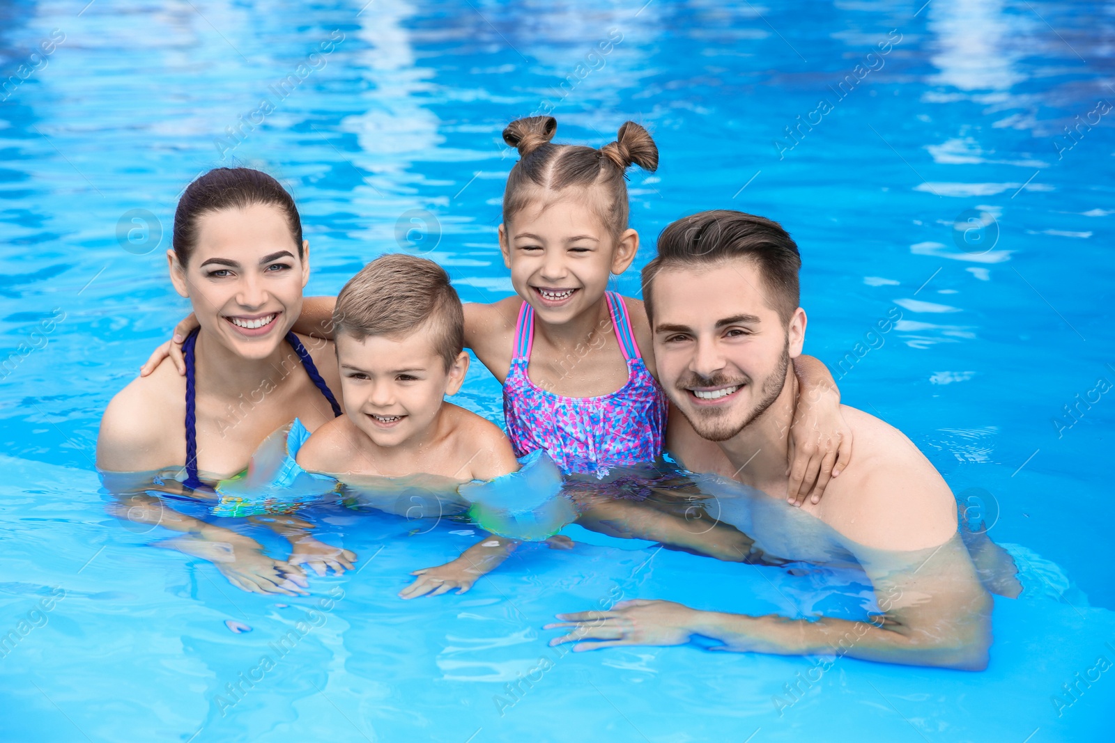 Photo of Young family with little children in swimming pool on sunny day