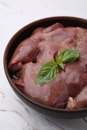 Photo of Bowl with raw chicken liver and basil on white textured table, closeup