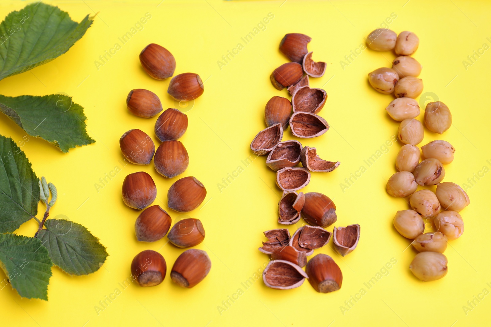 Photo of Flat lay composition with tasty organic hazelnuts and leaves on yellow background