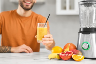 Handsome man with delicious smoothie at white marble table in kitchen, closeup