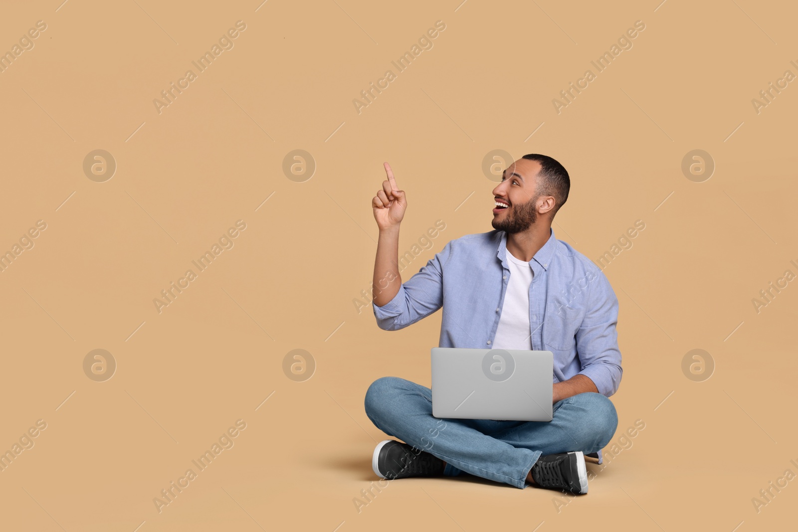 Photo of Smiling young man with laptop on beige background, space for text