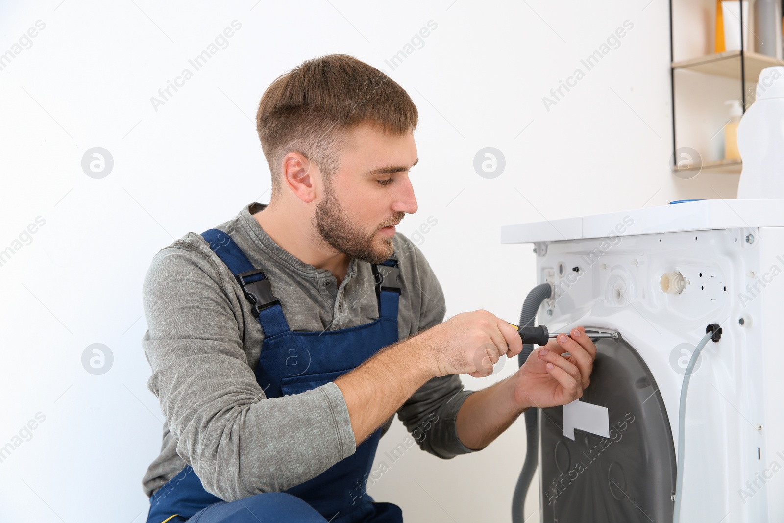 Photo of Young plumber fixing washing machine in bathroom