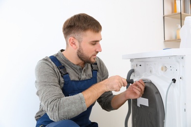 Young plumber fixing washing machine in bathroom