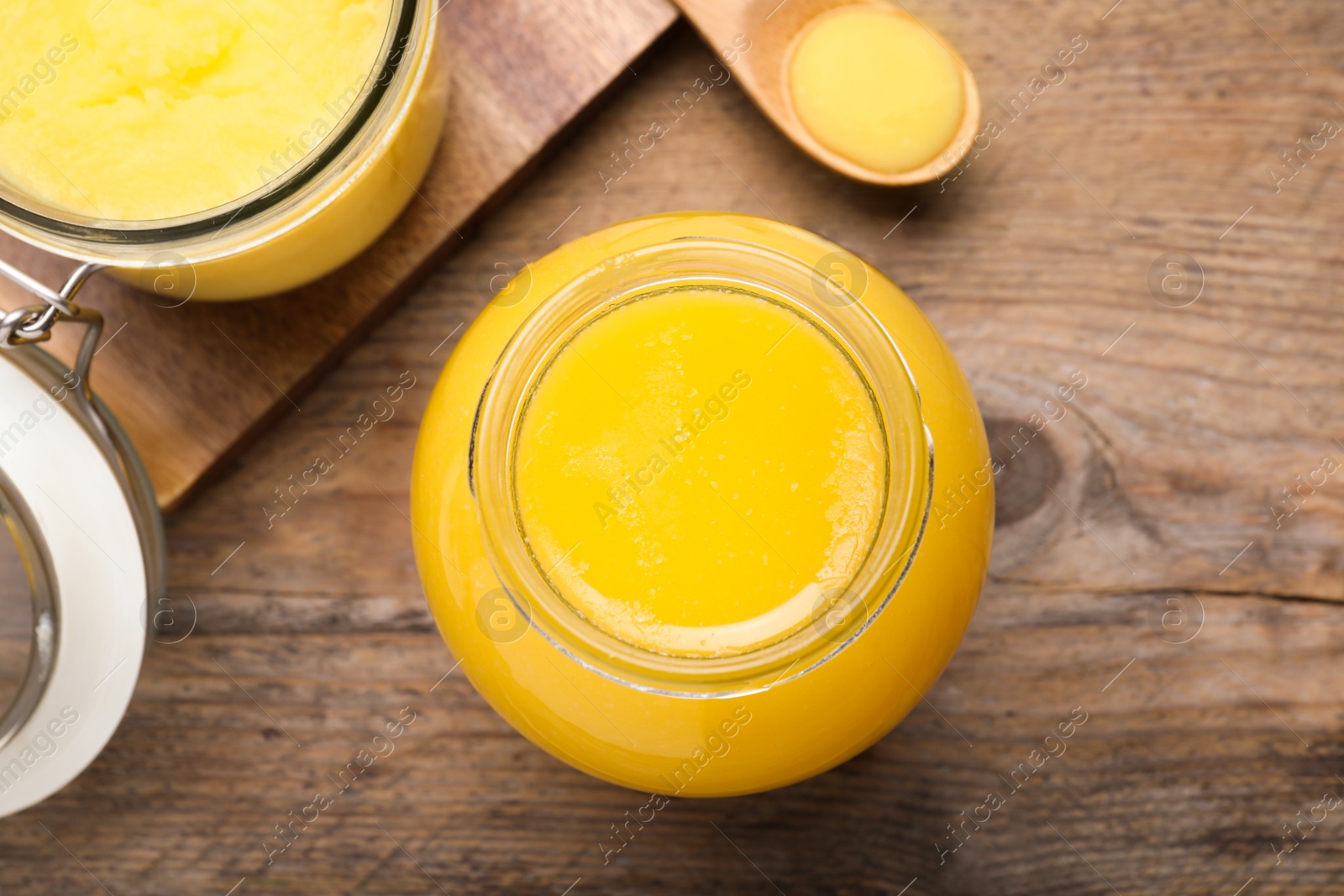 Photo of Glass jars and spoon of Ghee butter on wooden table, flat lay