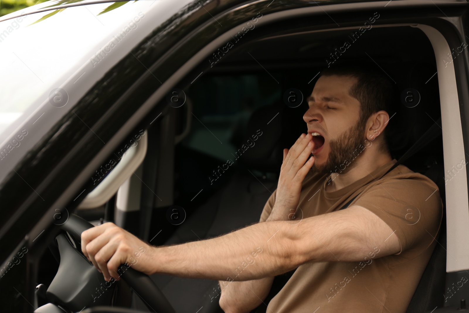 Photo of Tired man yawning while driving his modern car