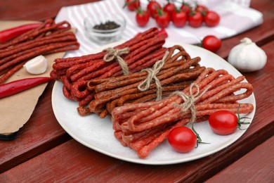 Photo of Bundles of delicious kabanosy with tomatoes on wooden table